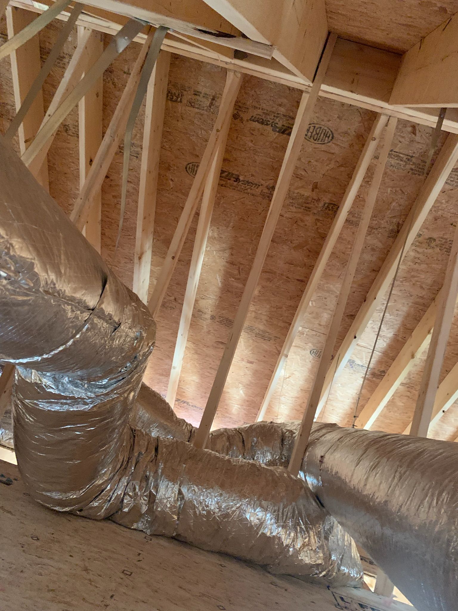 Interior view of an attic space with wooden rafters and silver HVAC ductwork.