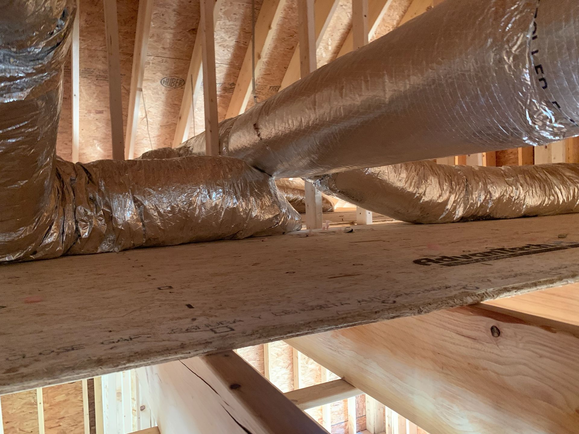 Inside unfinished attic, silver HVAC ductwork runs between wooden beams.