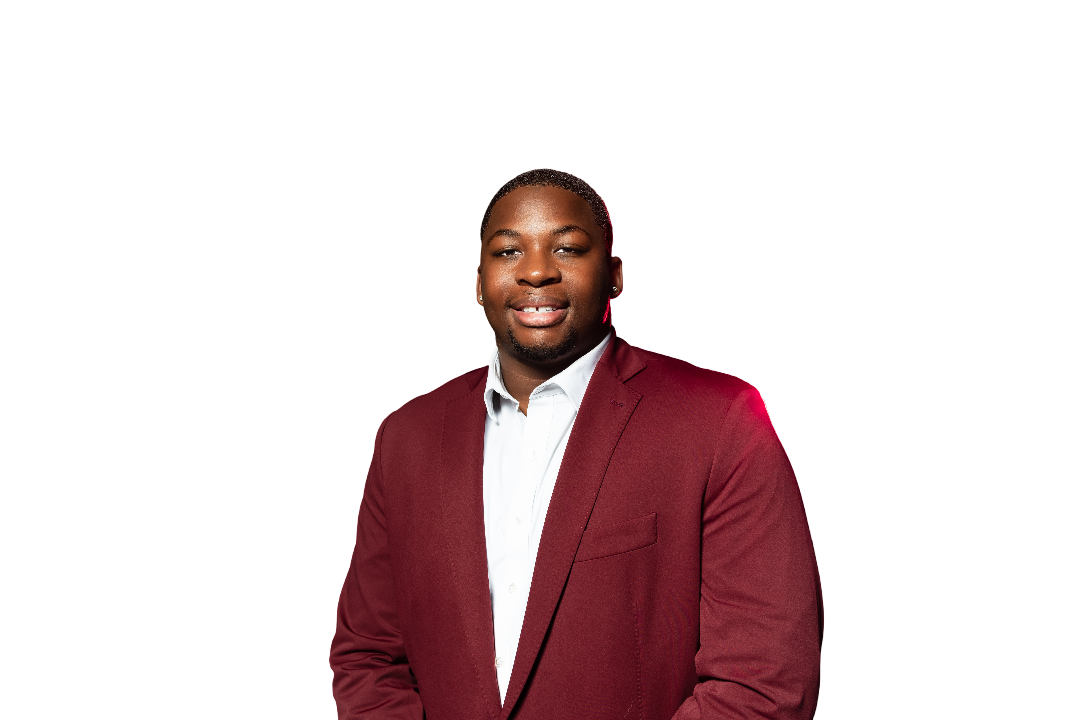 Man in maroon blazer and white shirt smiling at the camera, red lighting.