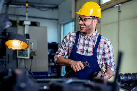 A man wearing a hard hat and safety glasses is working in a factory.