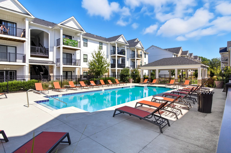 Outdoor swimming pool with lounge chairs on a concrete deck, next to a large residential apartment building.