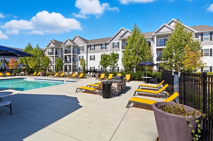 Outdoor swimming pool with lounge chairs on a concrete deck, next to a large residential apartment building.
