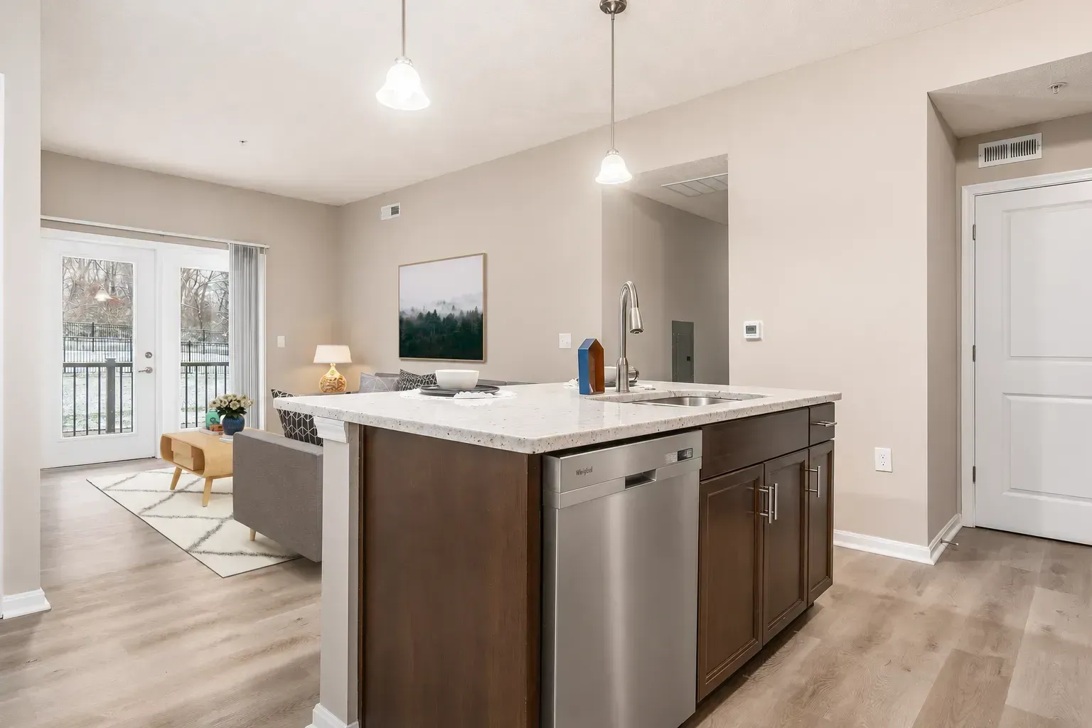 Modern kitchen with dark island, white countertops, pendant lights, and a glimpse of the living room and patio.