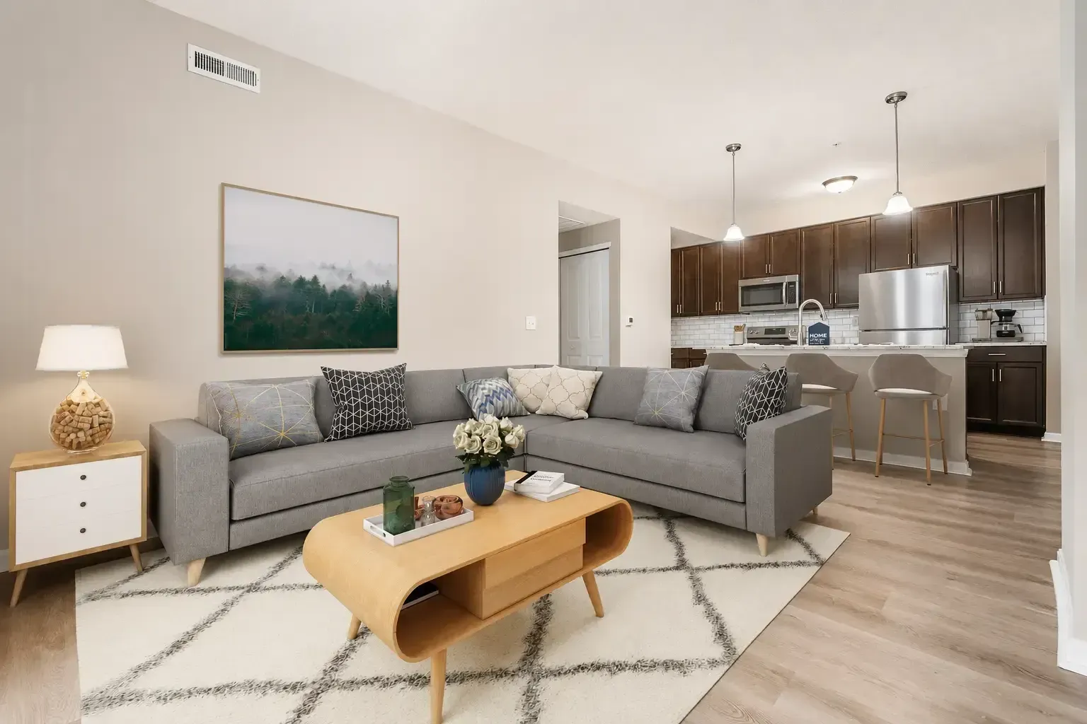 Modern living room with gray sectional, wood coffee table, rug, and open kitchen with bar stools