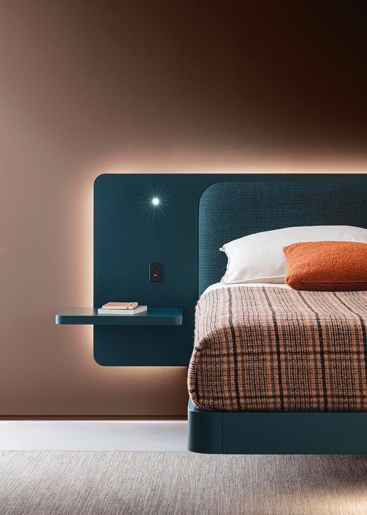 Letto imbottito color verde acqua con mensola sospesa e illuminazione integrata contro una parete color cuoio.