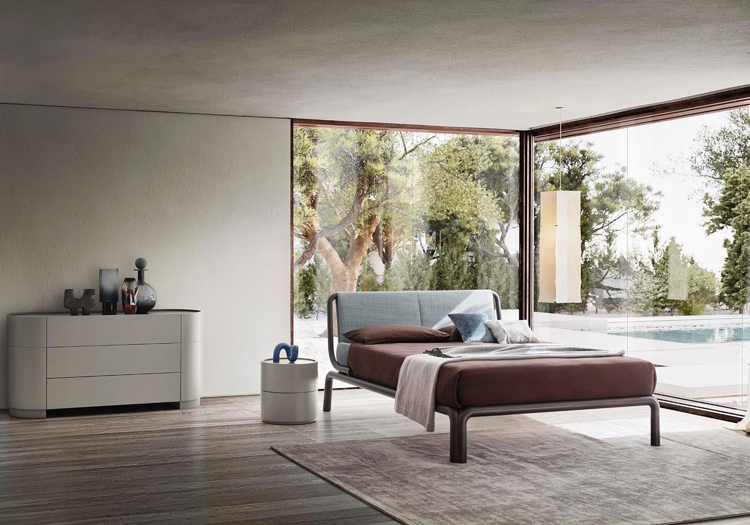 Camera da letto moderna con ampia finestra, letto, cassettiera, comodino e tappeto.