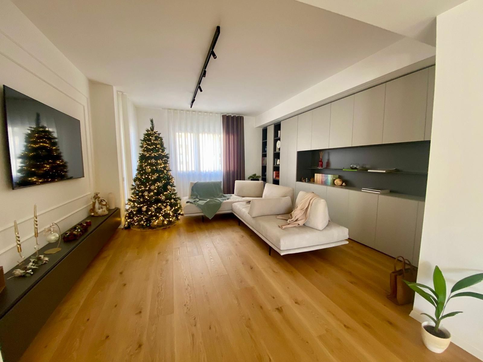 Soggiorno con albero di Natale, divano beige e pavimento in legno.