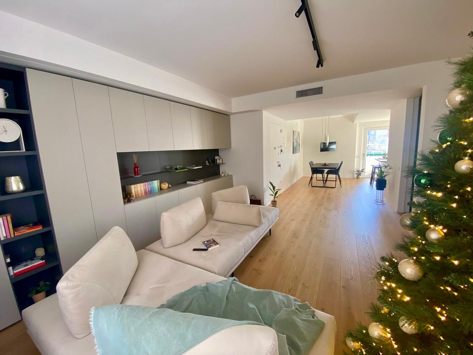 Soggiorno moderno con pavimenti in legno chiaro, divano e albero di Natale, che conduce alla zona pranzo.