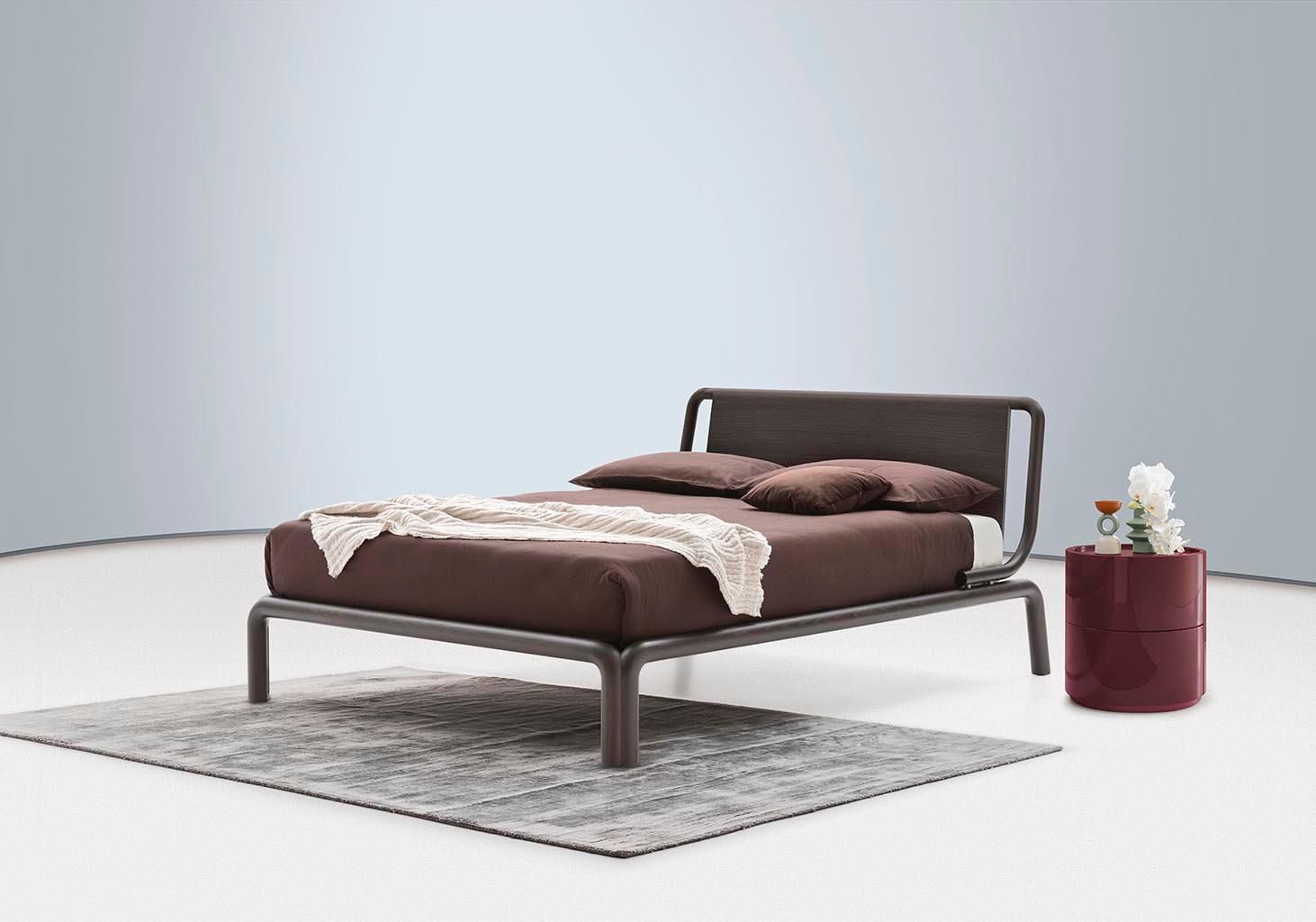 Letto marrone con testiera e comodino, appoggiato su un tappeto grigio.