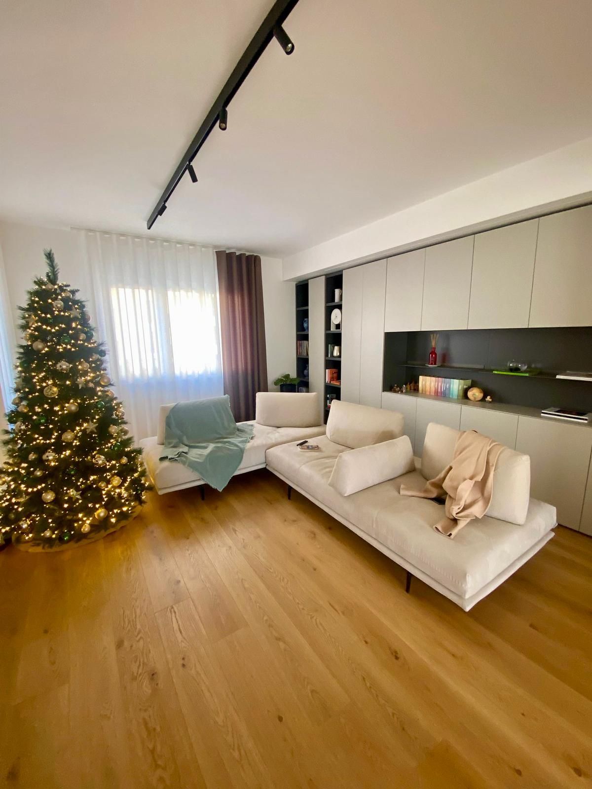 Un soggiorno moderno con un albero di Natale illuminato e un divano componibile bianco.