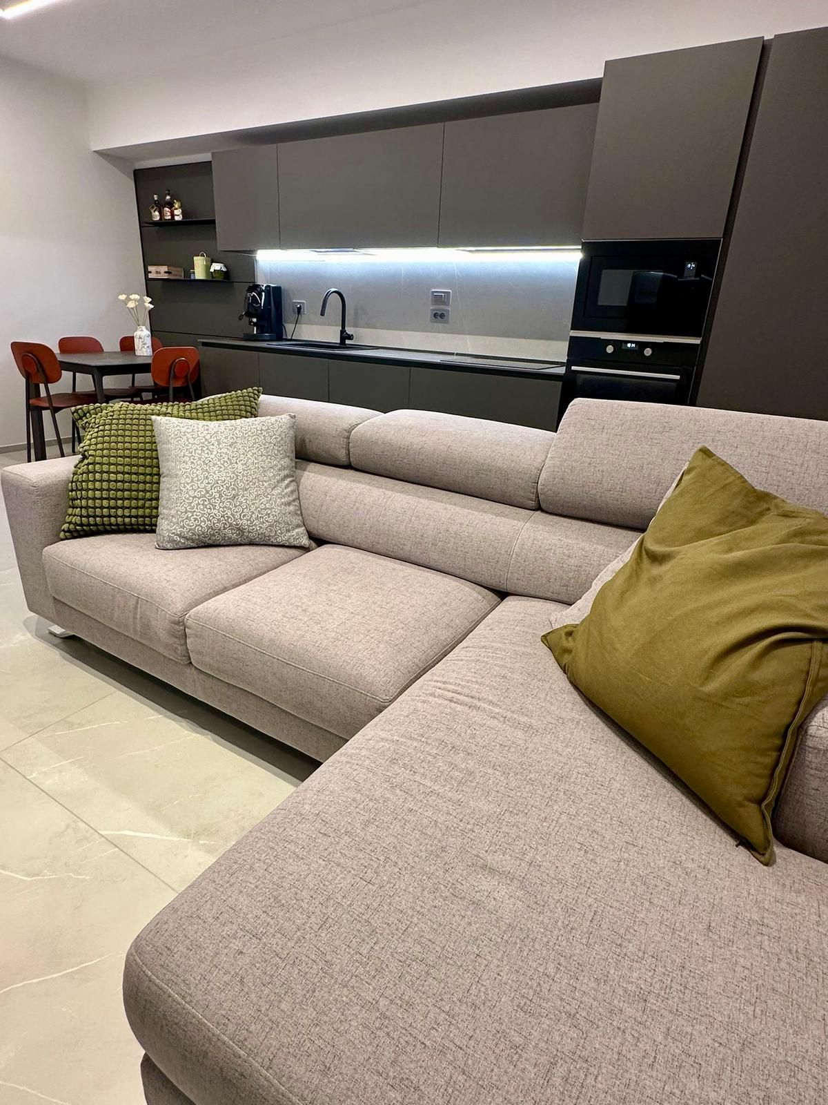 Divano componibile beige in una cucina moderna con mobili scuri, impreziosita da cuscini colorati.