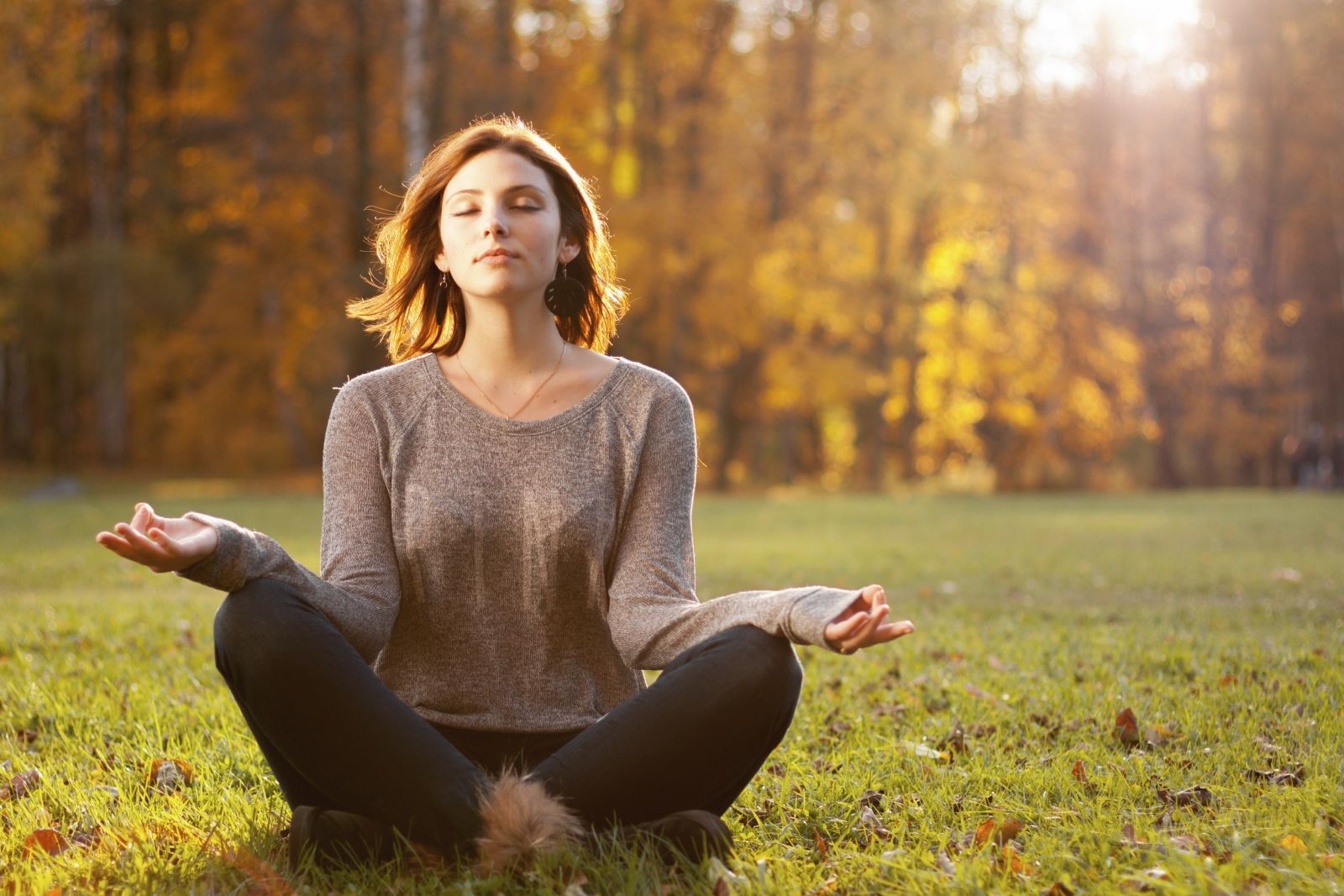 Woman meditating outdoors in a park with autumn foliage, eyes closed, hands in lotus position. We provide tools to help you manage anxiety and stress.