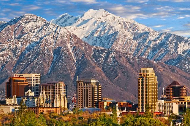 Salt Lake City skyline with snow-capped mountains in the background under a blue sky.