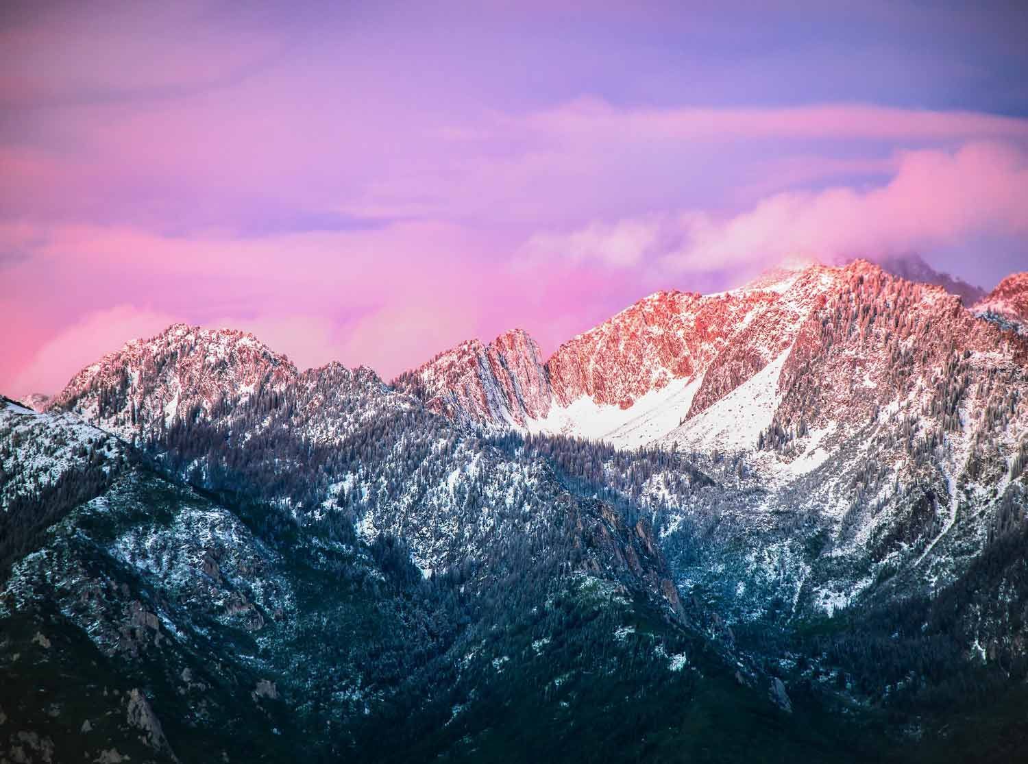 Snow-covered Wasatch mountain range at sunset with pink and orange hues.