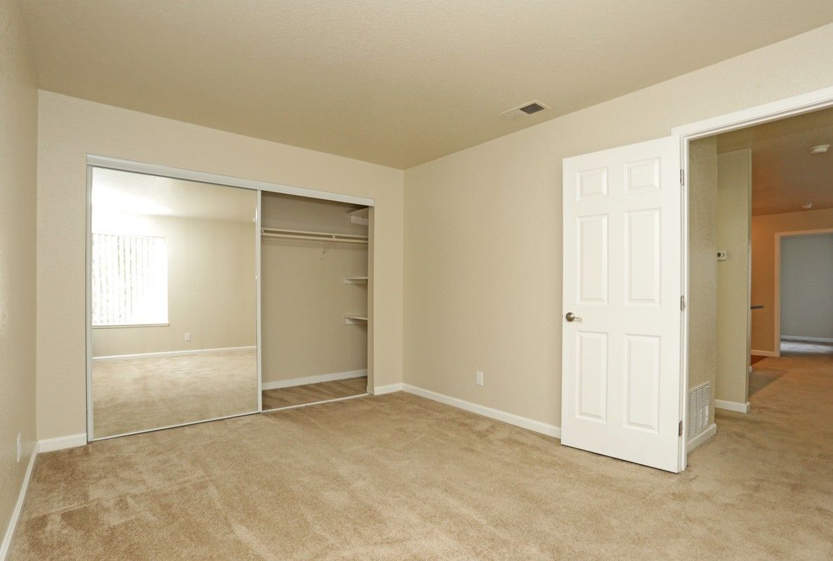 Empty bedroom with beige carpet, closet with sliding doors, and an open doorway.