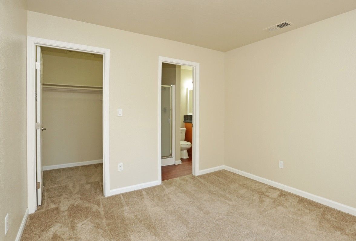 Beige bedroom with closet and bathroom entrances; light brown carpet.