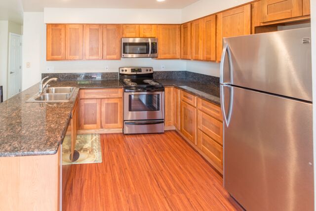 Kitchen with wood cabinets, stainless steel appliances, granite countertops, and wood flooring.