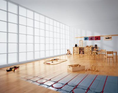 Ein Klassenzimmer mit Holzboden, der aufgeschnitten ist, um eine Fußbodenheizung mit Paneelen und Rohren freizulegen.