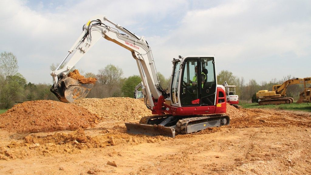 A red and white excavator is digging in a dirt field.