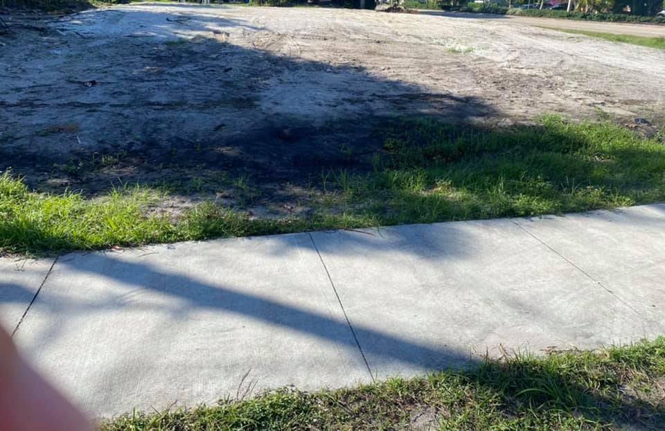 A sidewalk leading to a dirt road with grass on the side of it.