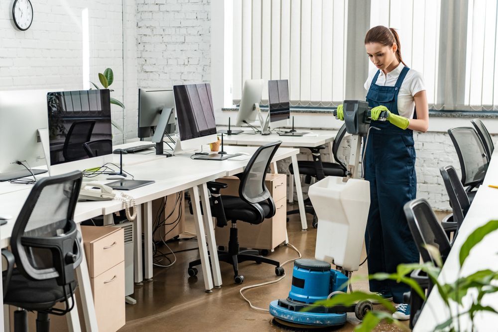 A woman is cleaning an office with a vacuum cleaner.