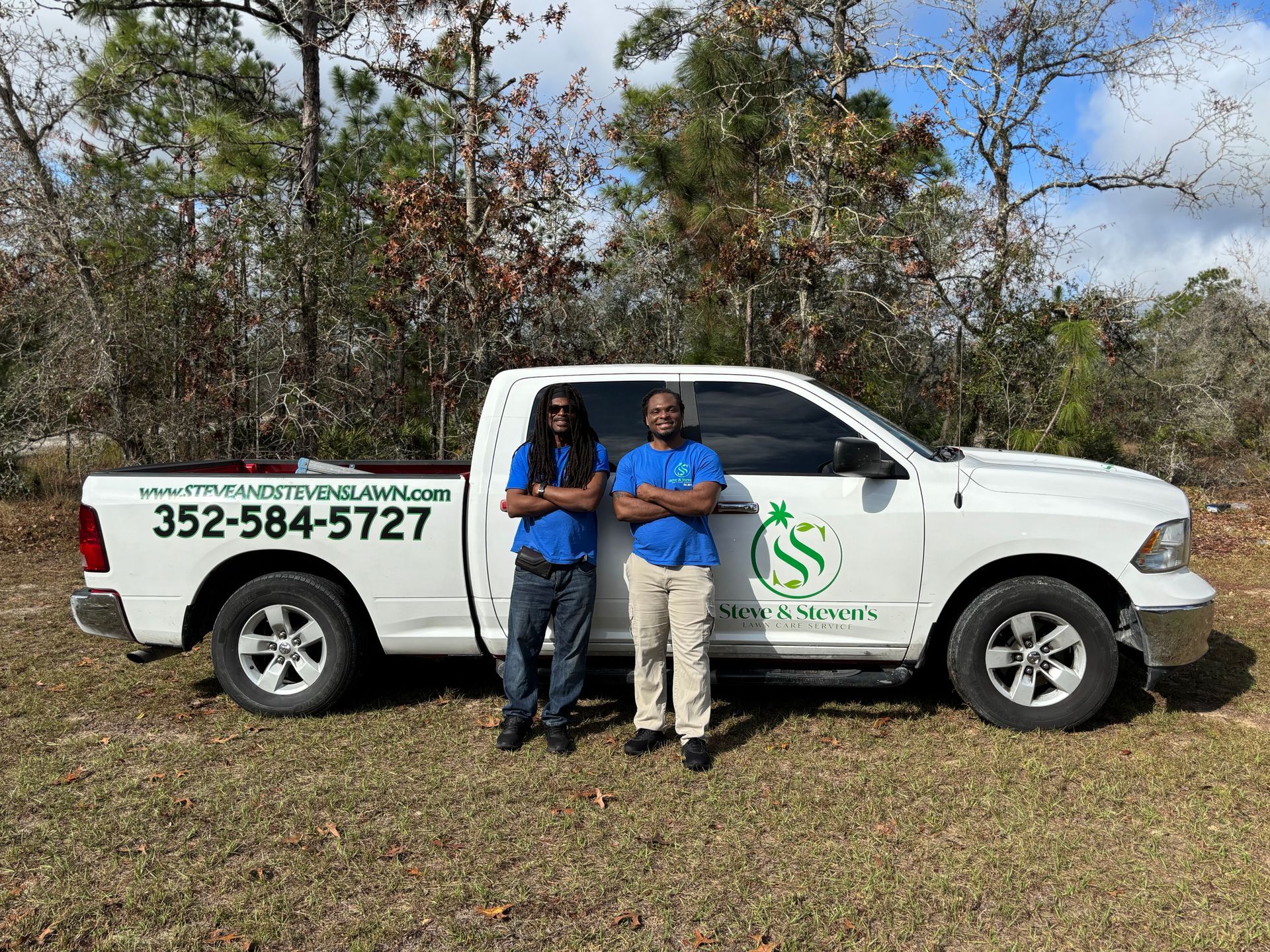 Two men are standing next to a white truck in a field.