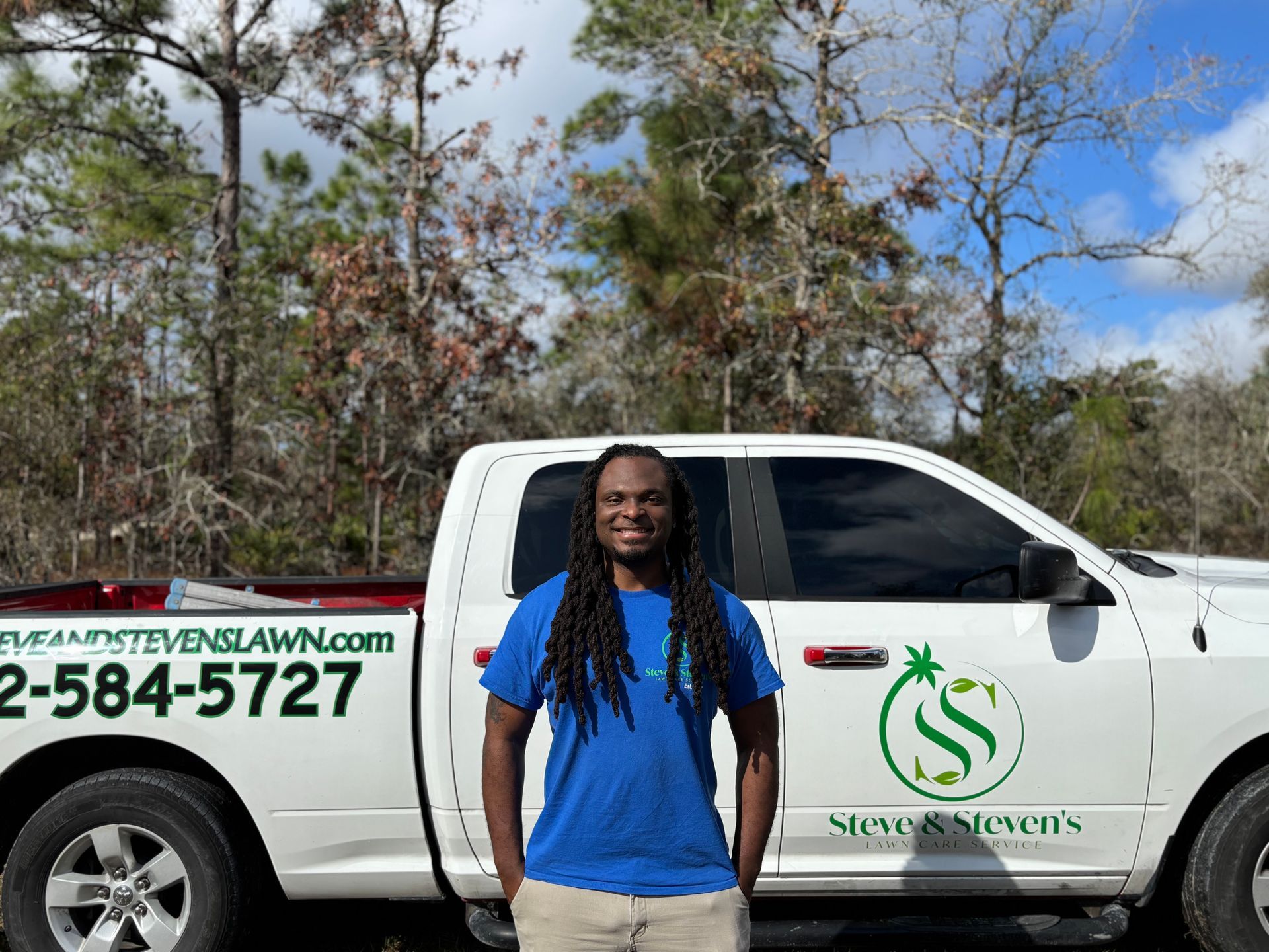 A man with dreadlocks is wearing a blue shirt that says steve & steven 's lawn care service.