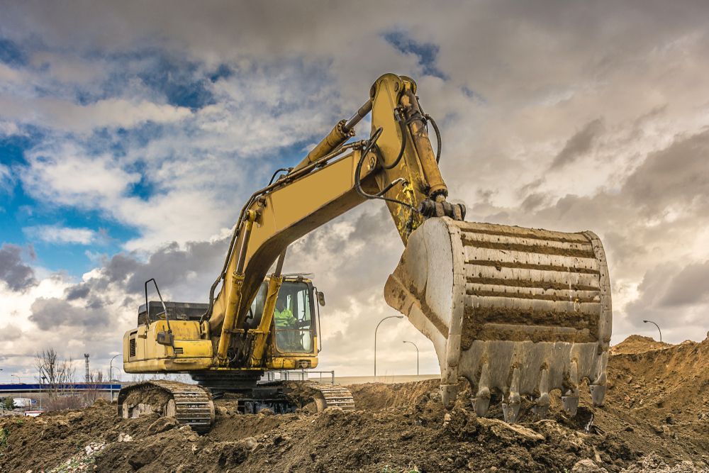 Yellow Excavator Digging Earth at a Construction Site Under a Cloudy Sky — Ace Clearing & Mulching In Nabiac, NSW