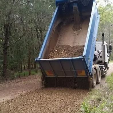 Dump Truck Unloading Gravel Onto a Dirt Road in a Wooded Area — Ace Clearing & Mulching In Old Bar, NSW