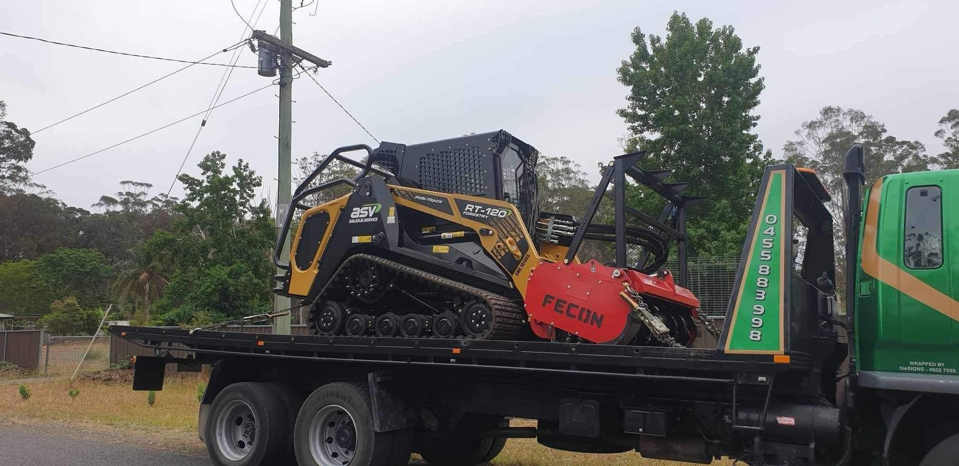 A Small Tracked Skid Steer With a Brush Cutter Loaded on a Flatbed Truck — Ace Clearing & Mulching In Old Bar, NSW