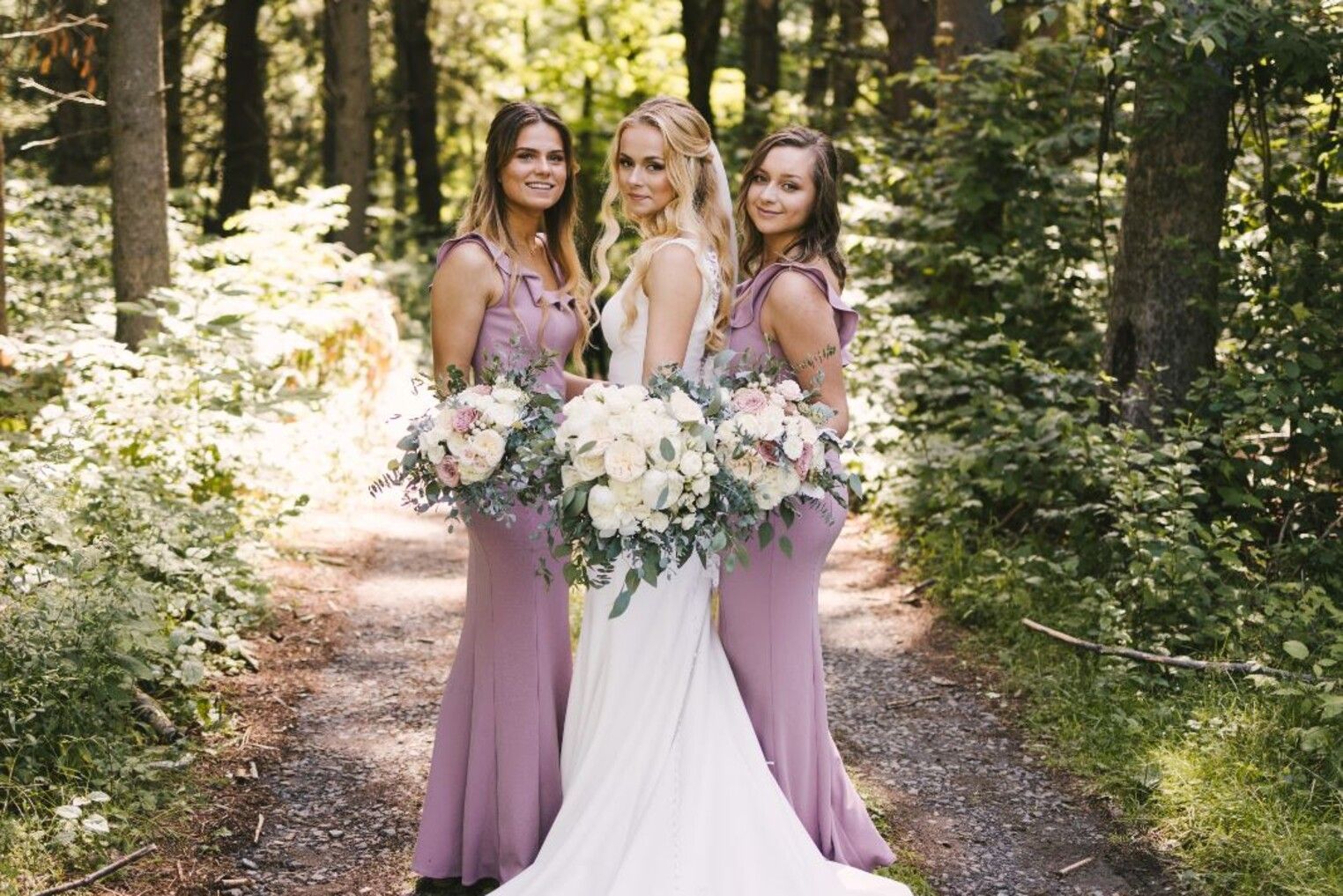 A bride and her bridesmaids are posing for a picture in the woods.