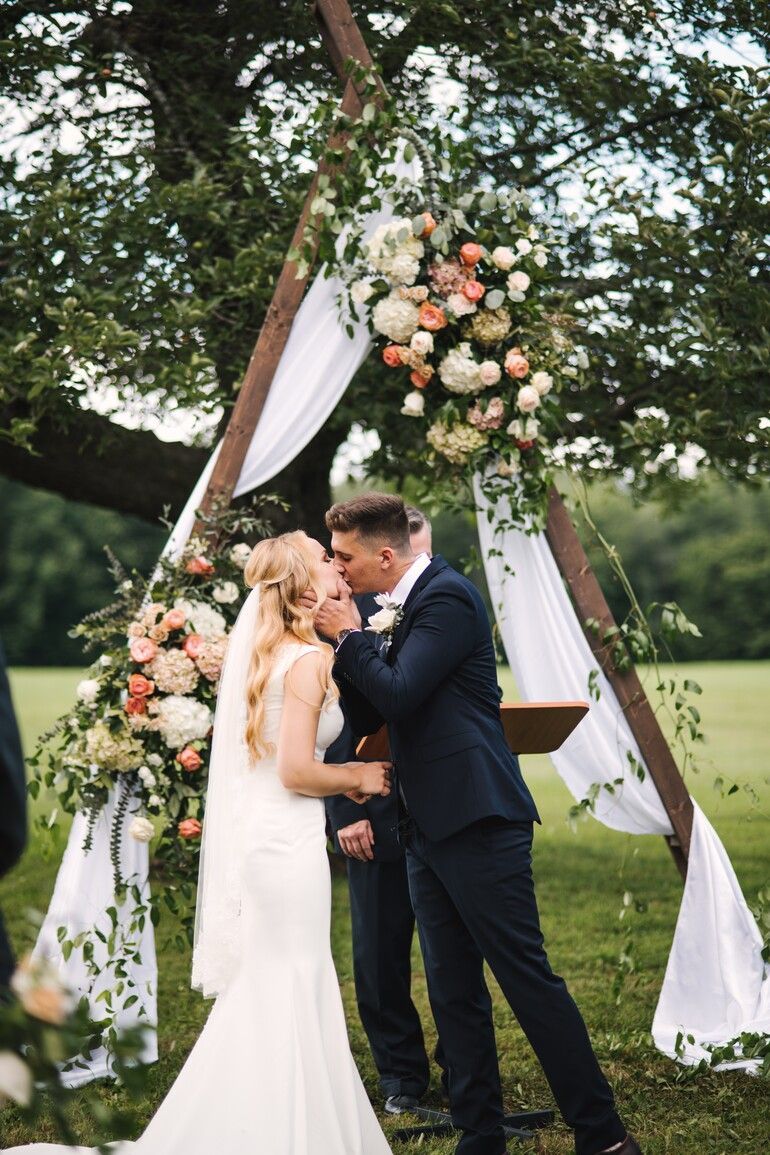 A bride and groom kissing under a wooden arch at their wedding ceremony.