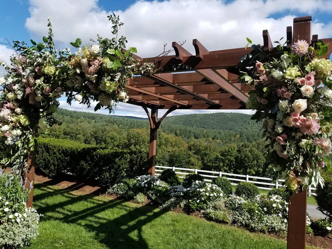 A wooden pergola decorated with flowers is sitting on top of a lush green field.