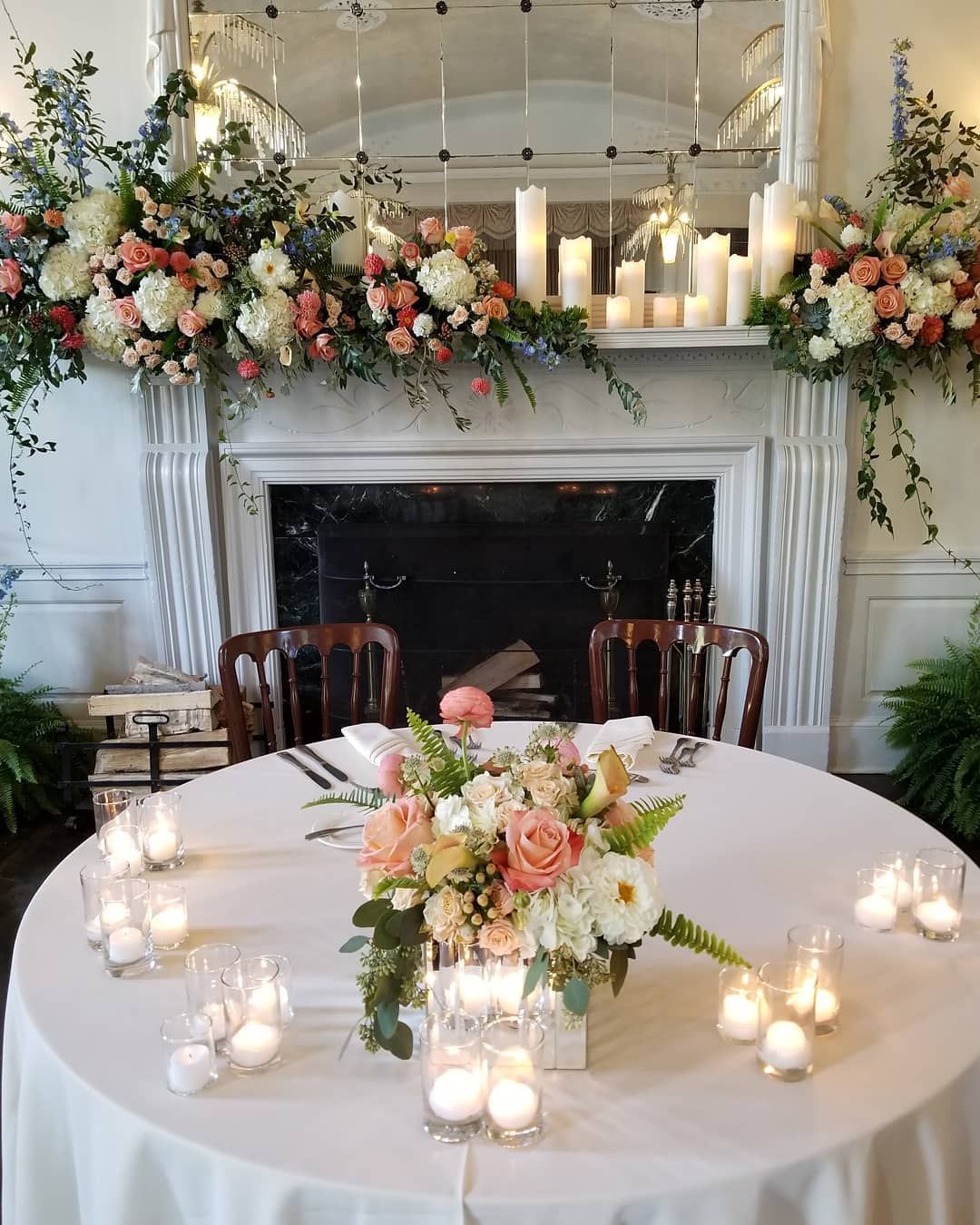 A table with flowers and candles on it in front of a fireplace