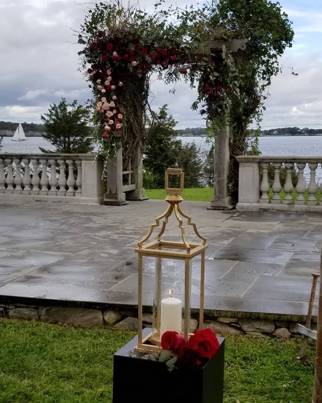 A lantern with a candle inside of it is sitting in front of a floral arch.