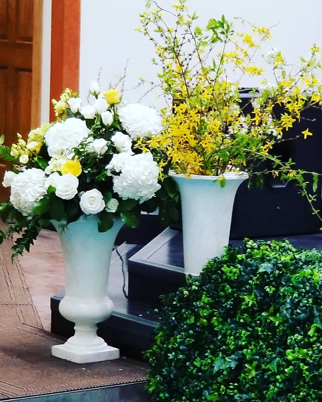 Two white vases filled with white flowers and yellow flowers