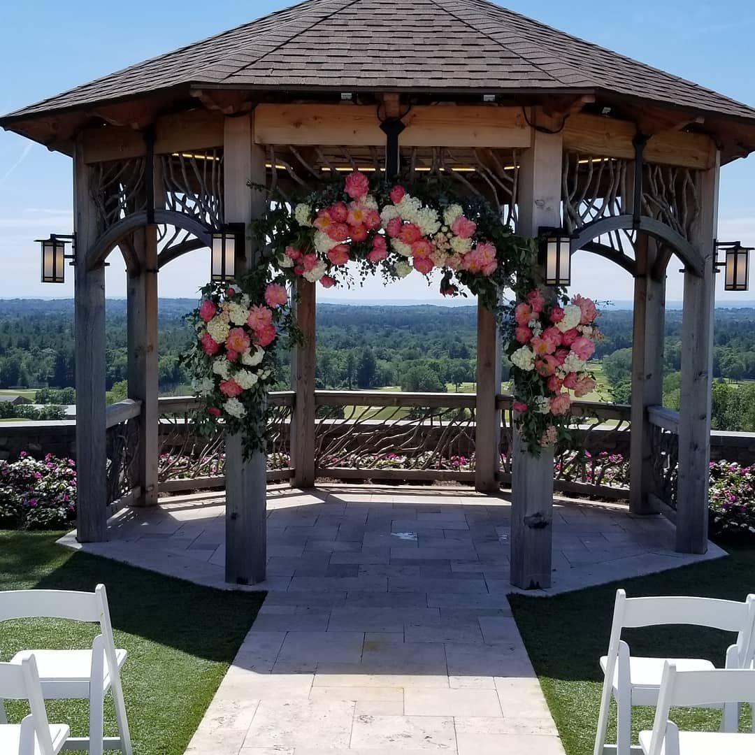 A gazebo decorated with pink and white flowers and white chairs