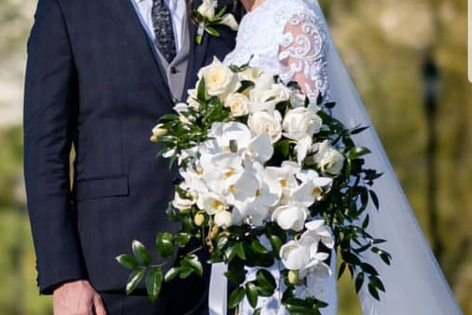 A bride and groom are posing for a picture while the bride is holding a bouquet of white flowers.