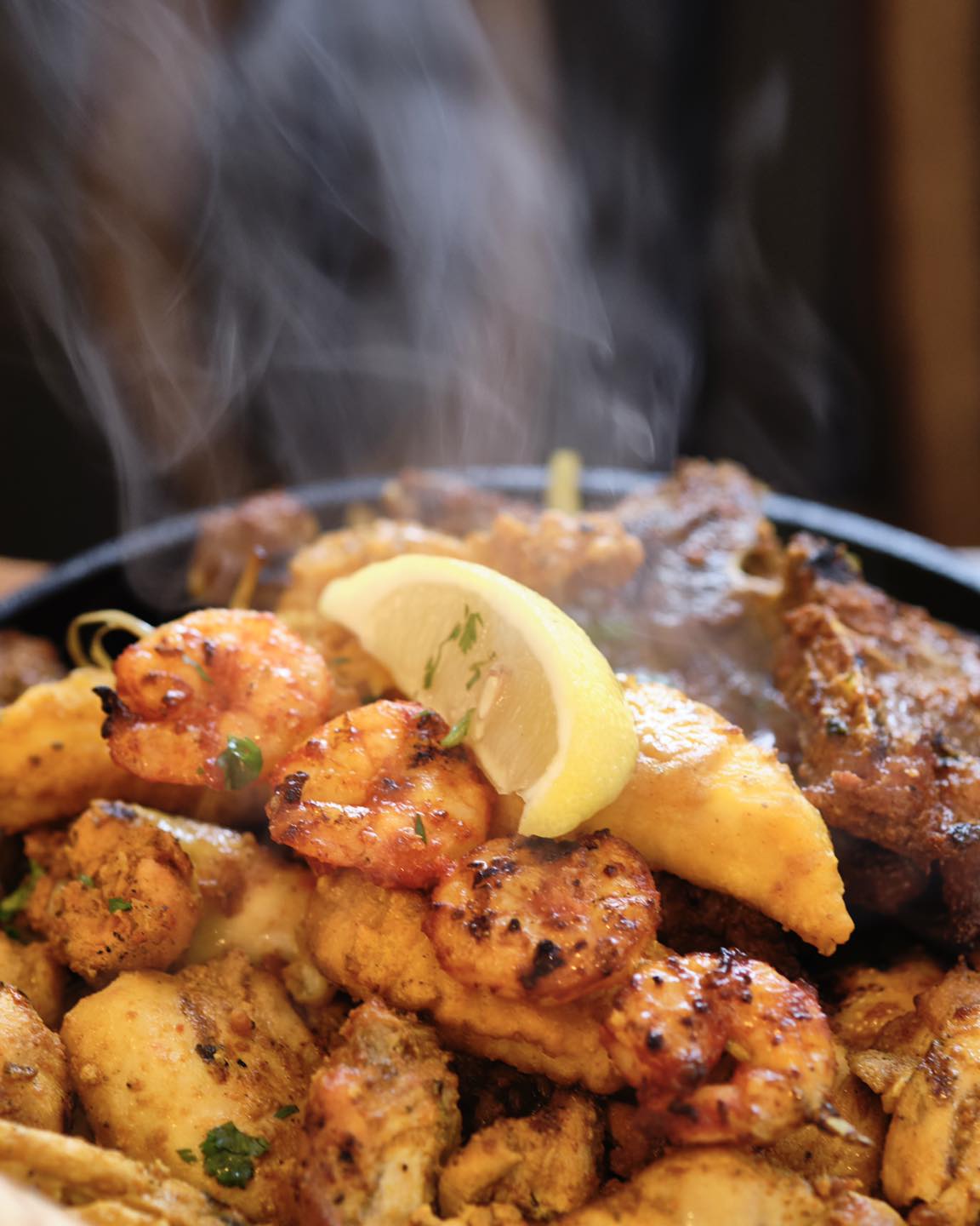 Steaming platter of grilled seafood and chicken, garnished with lemon.