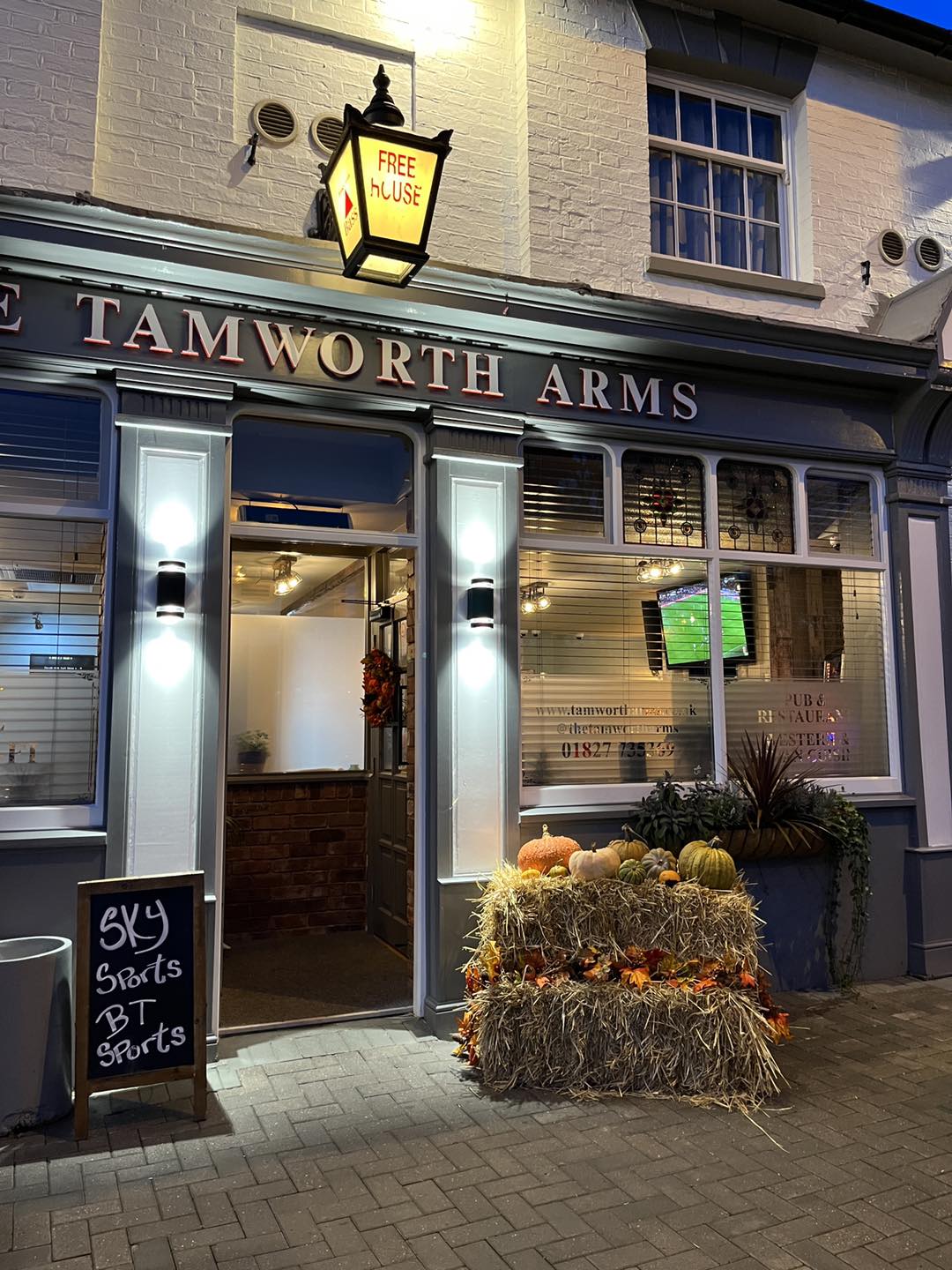 Exterior of the Tamworth Arms pub at night, with a hanging lantern, pumpkins, and a sign for Sky and BT Sports.