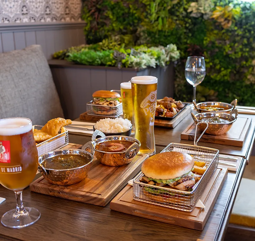 Table with pub food: burgers, curry, fries, beer, and water in a restaurant.