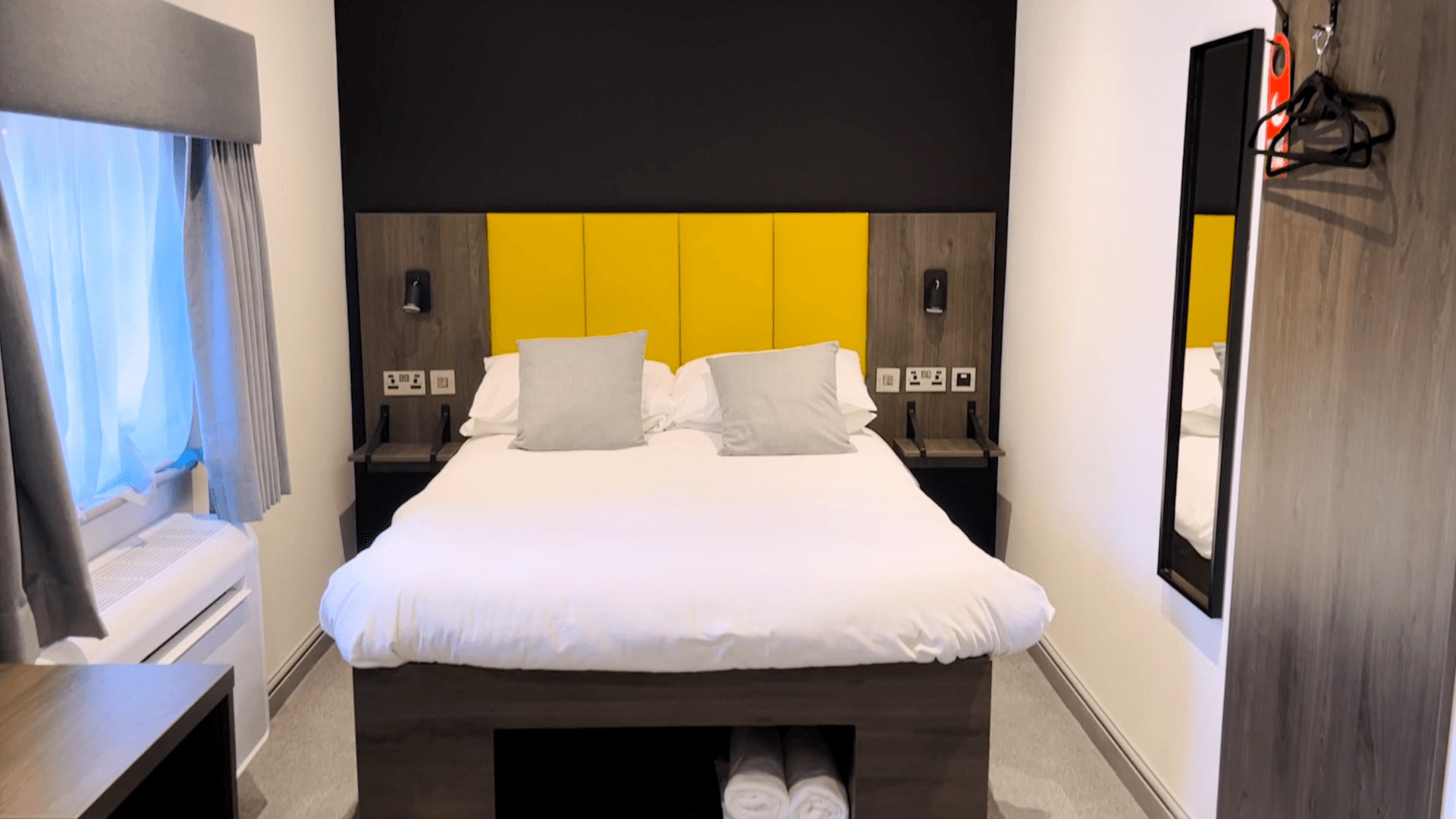 Hotel room with a bed, nightstands, and a yellow headboard, black wall and mirror.