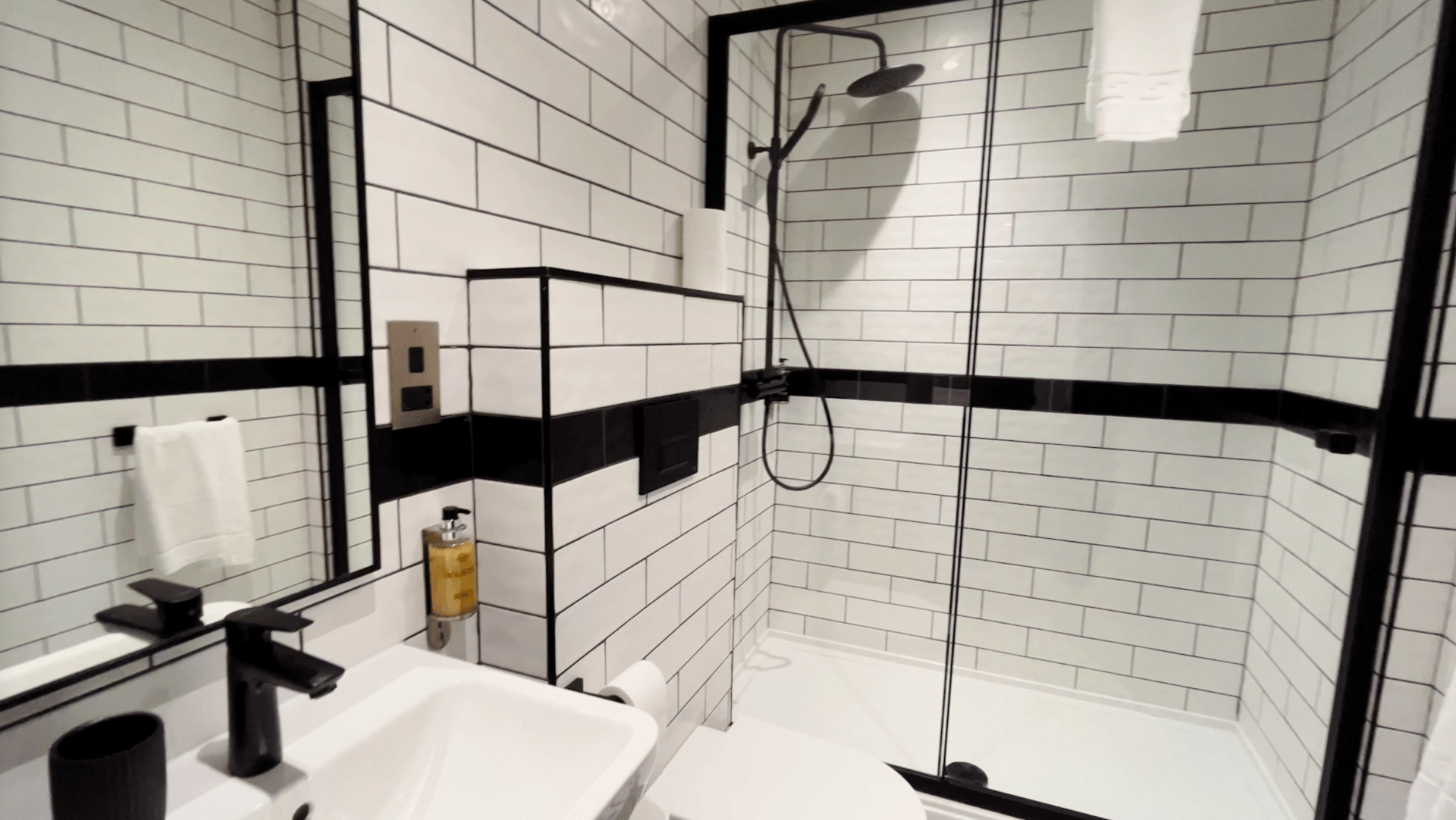 Modern bathroom with white subway tiles, black trim, glass shower, and black fixtures.