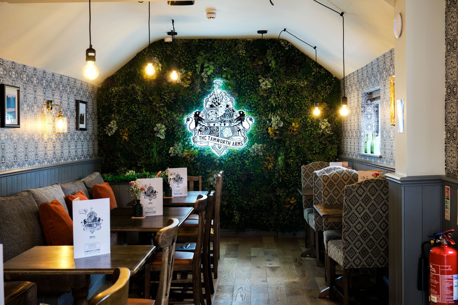 Cozy restaurant interior with wooden tables, booths, and a decorative moss wall with a neon sign.
