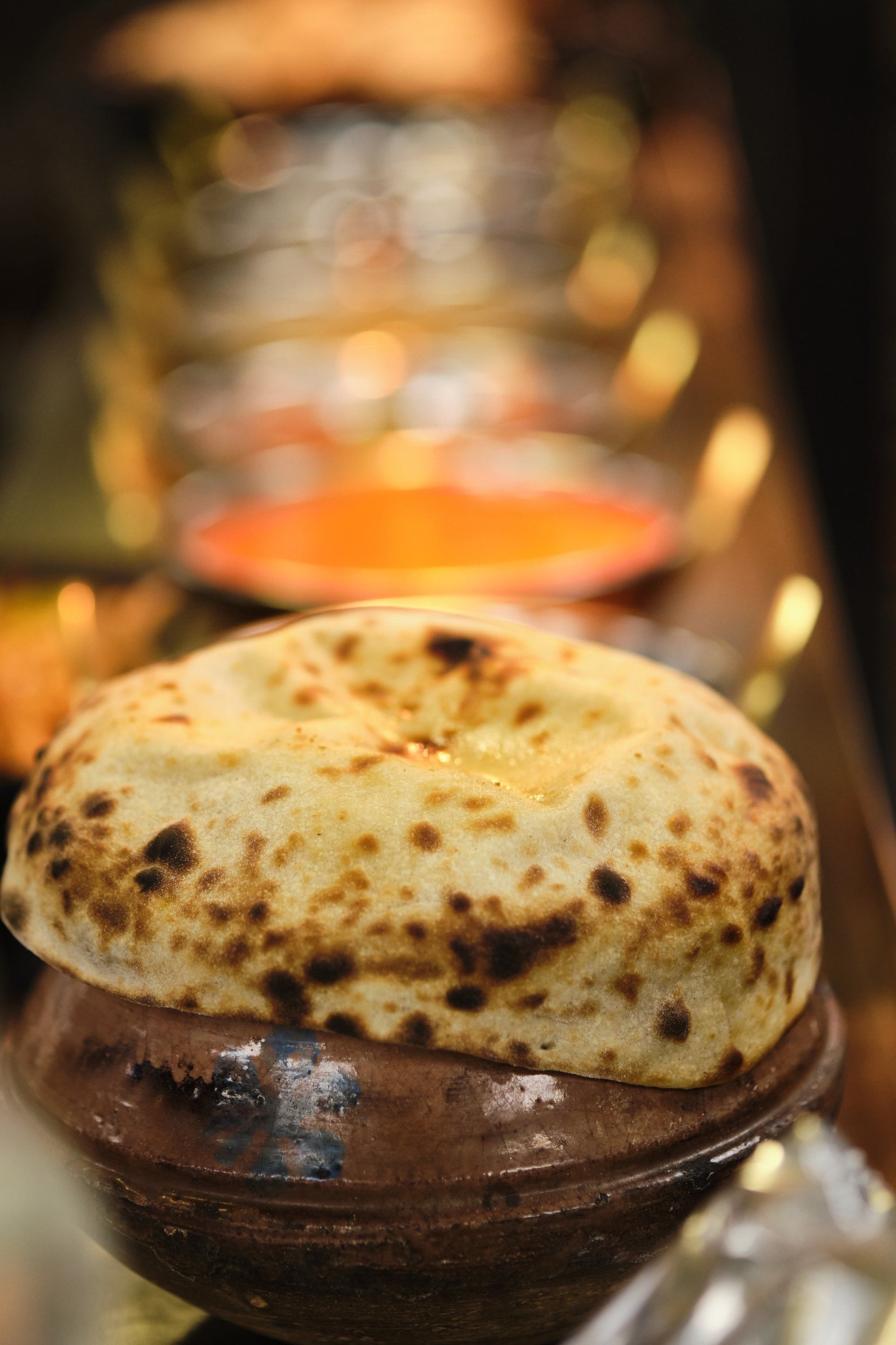 Clay pot of food sealed with baked bread. Blurred background with other dishes.