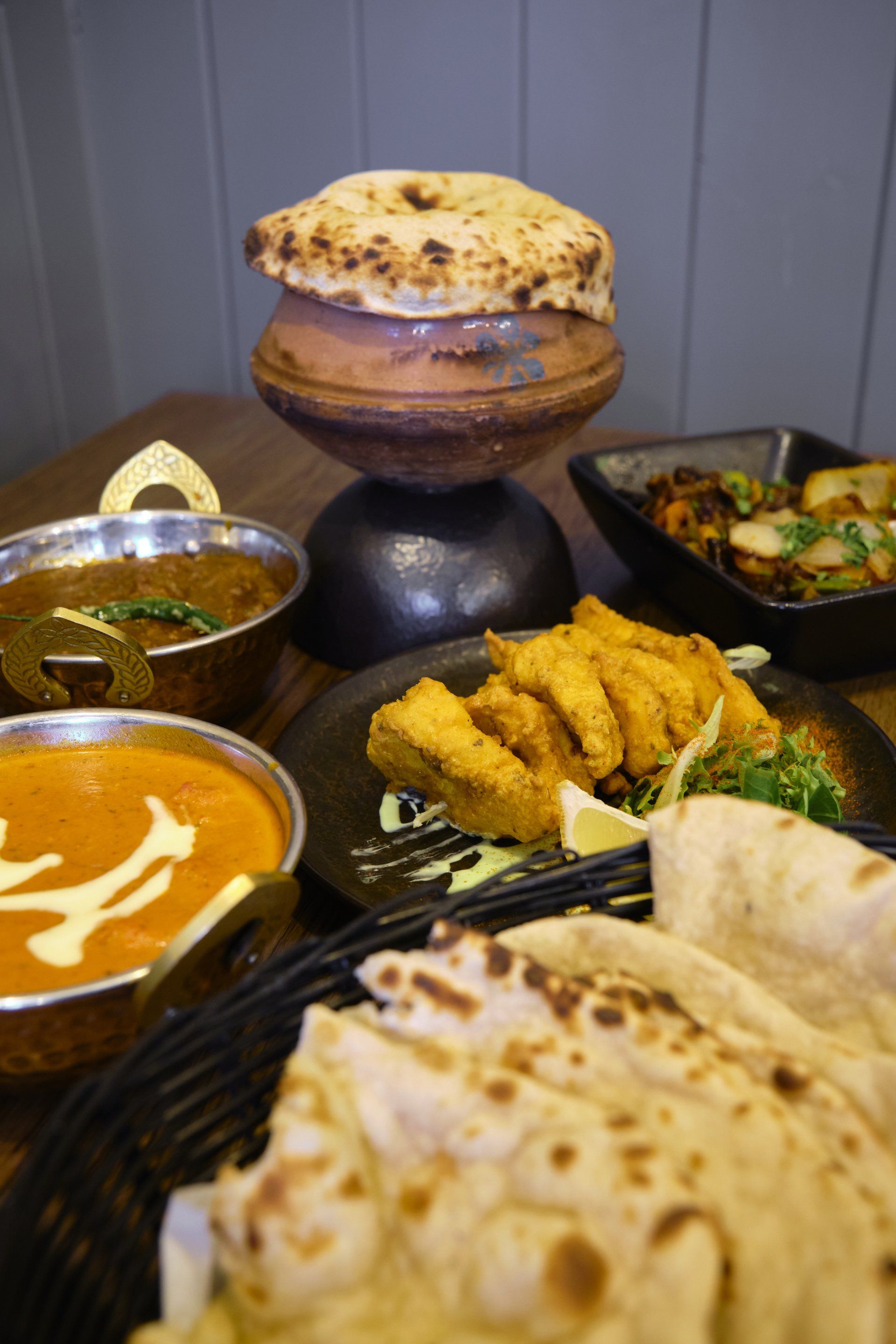 Indian food spread: curry in bowls, fried items, naan, clay pot with bread.