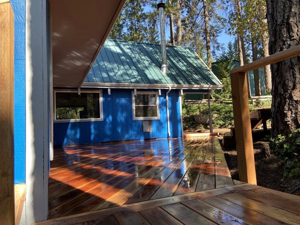 Blue cabin with teal roof and wooden deck surrounded by trees.
