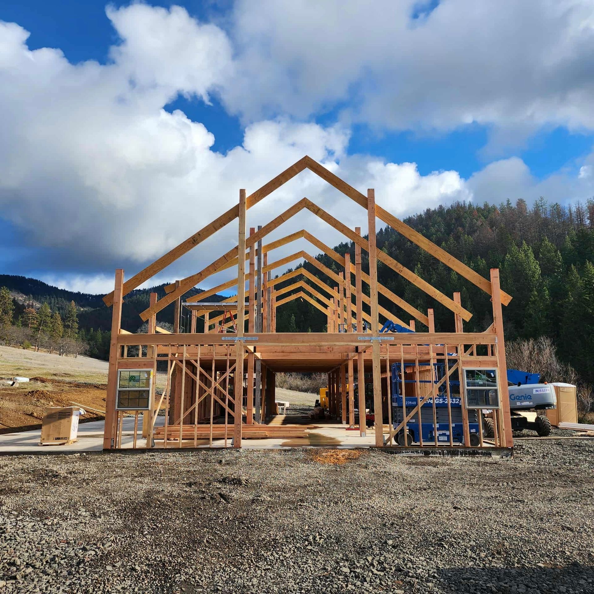 Wooden building frame under construction, blue sky with clouds, surrounded by a gravel lot.