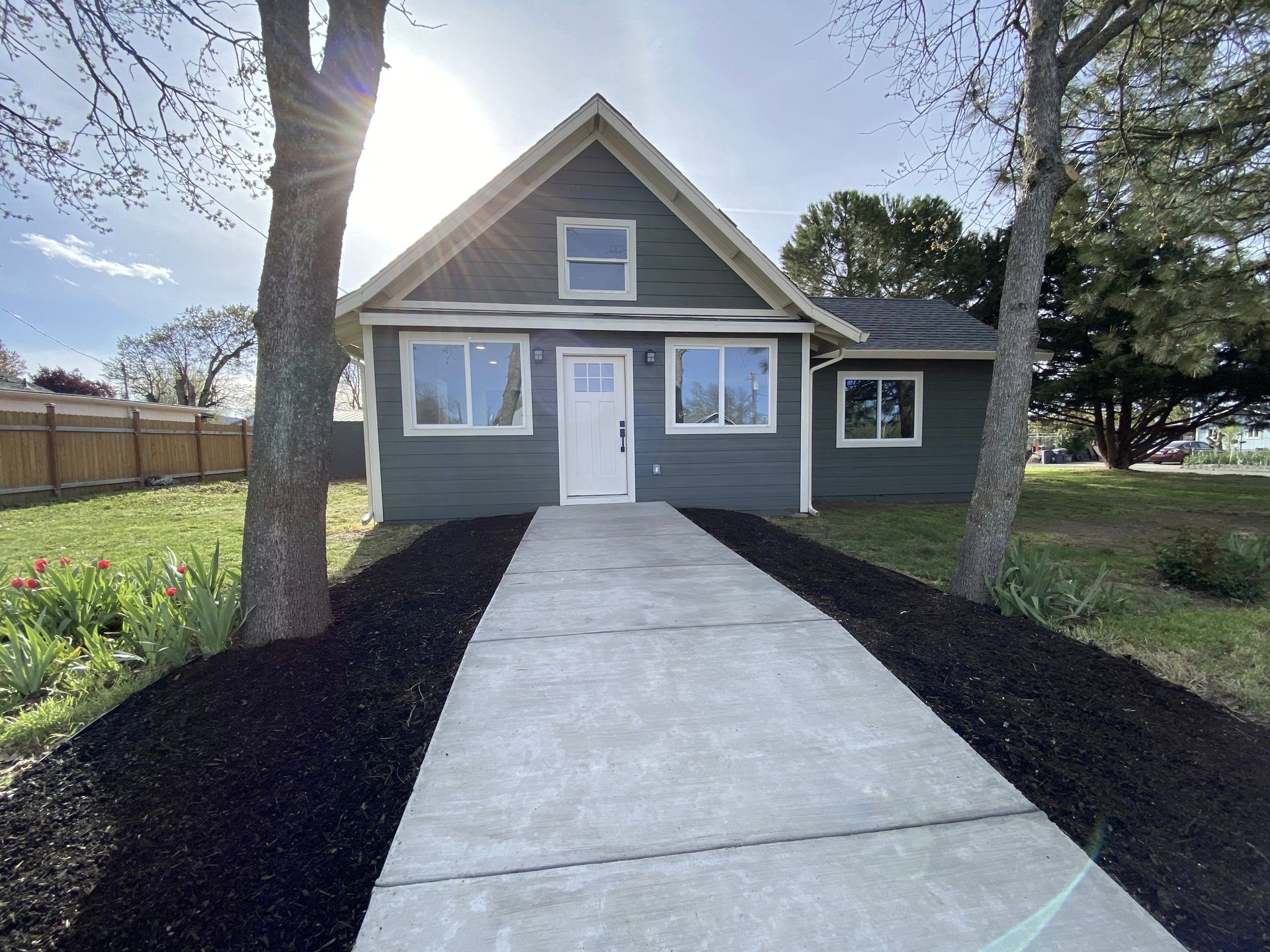 Green house with white door, walkway, two trees, and mulch landscaping.