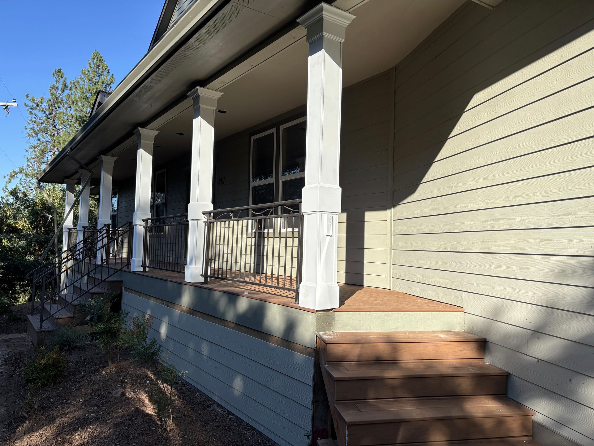 Porch with white columns, brown stairs, and a metal railing. The house has light green siding.